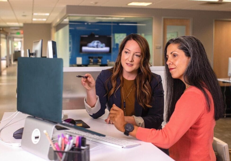 Two women sitting at a table looking at a computer screen.